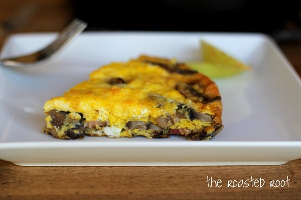 A slice of mushroom frittata with visible mushrooms sits on a white plate, accompanied by a small wedge of green apple. A fork rests in the background. The words the roasted root appear in the corner.