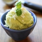 A scoop of basil coconut milk ice cream, garnished with coconut flakes and a fresh basil leaf, served in a small blue bowl on a wooden surface.