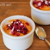 Two white ramekins filled with orange pudding or mousse, reminiscent of butternut squash soup, are topped with grated red beet and white sprinkles on a wooden surface with a silver spoon. The Roasted Root appears in the top left corner.