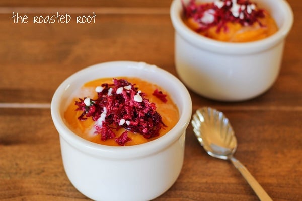 Two white ramekins filled with orange pudding or mousse, reminiscent of butternut squash soup, are topped with grated red beet and white sprinkles on a wooden surface with a silver spoon. The Roasted Root appears in the top left corner.