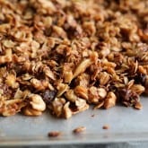 A close-up view of homemade date granola with oats, nuts, and dried fruit spread out on a baking sheet.