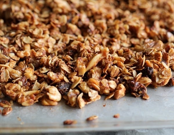 A close-up view of homemade date granola with oats, nuts, and dried fruit spread out on a baking sheet.