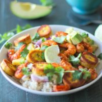 A vibrant Cuban Shrimp Bowl filled with rice, grilled shrimp, fried plantains, avocado chunks, pineapple, red onion, fresh cilantro, and a lime wedge—all arranged in a colorful, appetizing presentation.