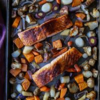 Sheet pan salmon fillets rest on a baking sheet, surrounded by an assortment of roasted vegetables—carrots, sweet potatoes, onions, and parsnips—for a colorful and wholesome meal.