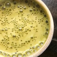 A close-up of a ceramic cup filled with frothy, bulletproof matcha tea, its surface covered in tiny bubbles, elegantly set on a dark, reflective surface.