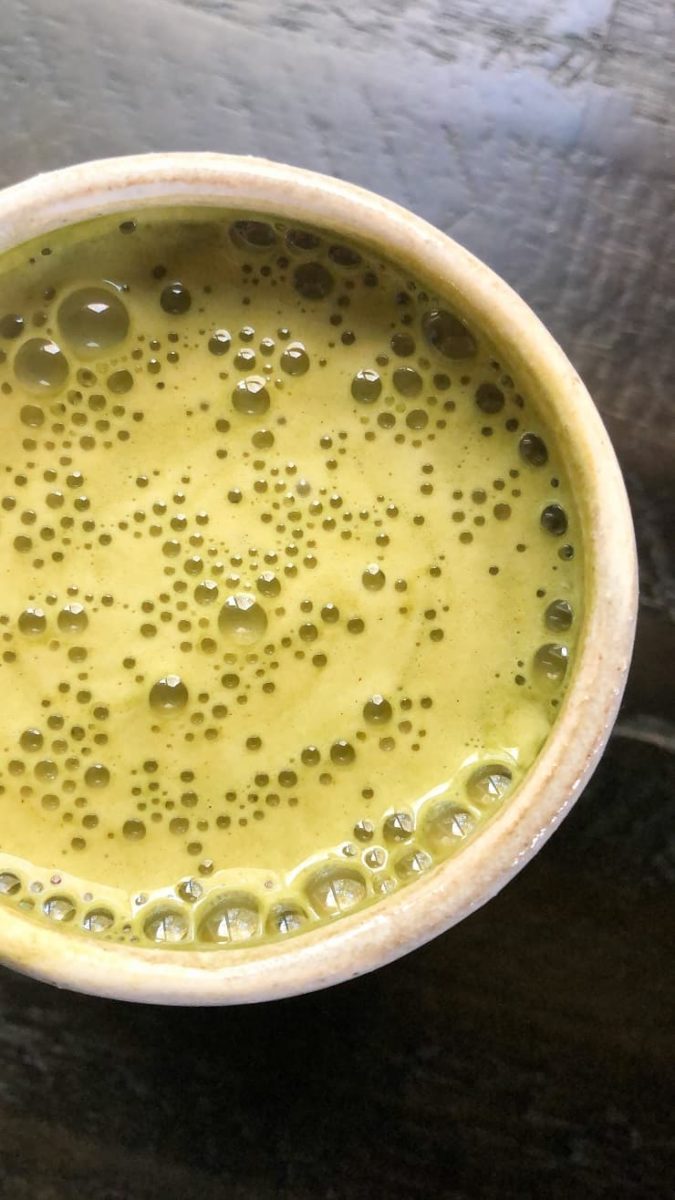 A close-up of a ceramic cup filled with frothy, bulletproof matcha tea, its surface covered in tiny bubbles, elegantly set on a dark, reflective surface.