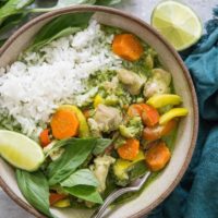 Bowl of green curry with rice and a blue napkin to the side with a lime wedge and fresh basil.