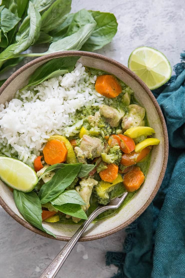 Bowl of green curry with rice and a blue napkin to the side with a lime wedge and fresh basil.