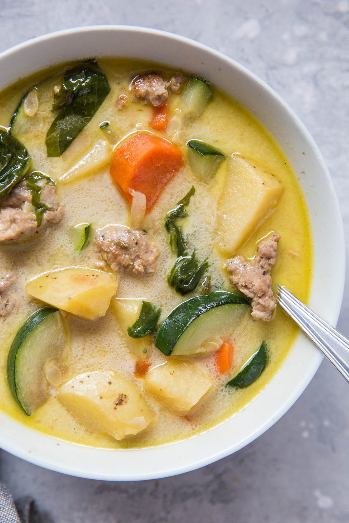 Close up top down image of a big white bowl of ground turkey soup with veggies and creamy broth.