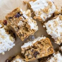 Sliced pieces of low-carb carrot cake topped with white frosting and chopped walnuts, showing a moist, crumbly texture with visible bits of carrot and raisins, arranged on parchment paper.