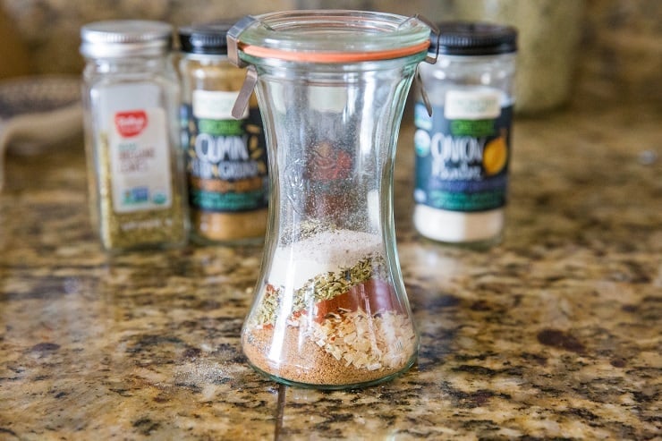 Jar full of homemade taco seasoning and individual jars full of spices in the background.