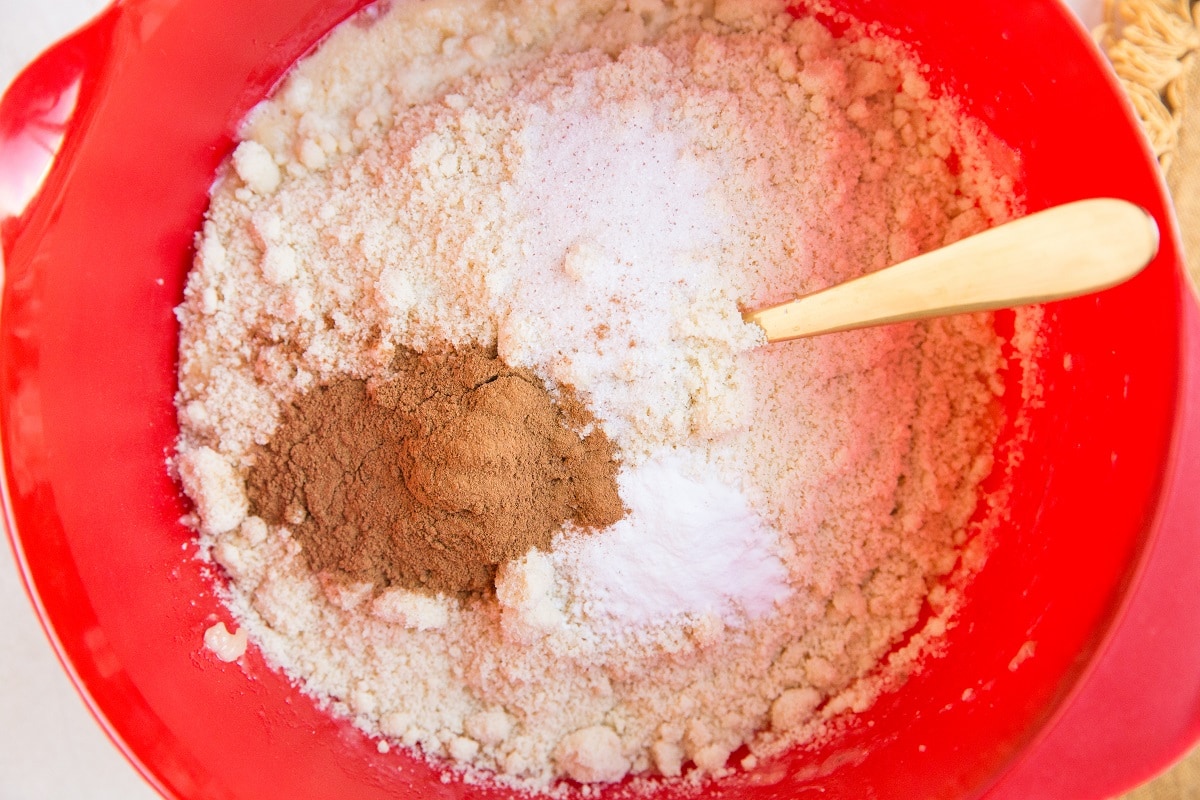 A red mixing bowl containing flour, baking powder, cinnamon, and salt with a wooden spoon resting inside—perfect for making Healthy Carrot Cake Muffins or even Paleo Carrot Cake Muffins.