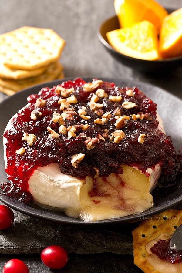 The easiest snack you can make for entertaining holiday guests โ Cranberry Baked Brie served on a festive cheese board with crackers and fruit. Great recipe to use up leftover cranberry sauce. Ooey gooey cheese ready in 10 minutes!
