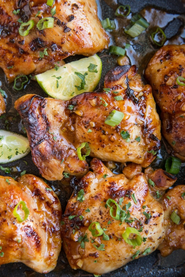 Close up image of Asian Boneless Baked Chicken Thighs with green onion sprinkled on top and some limes