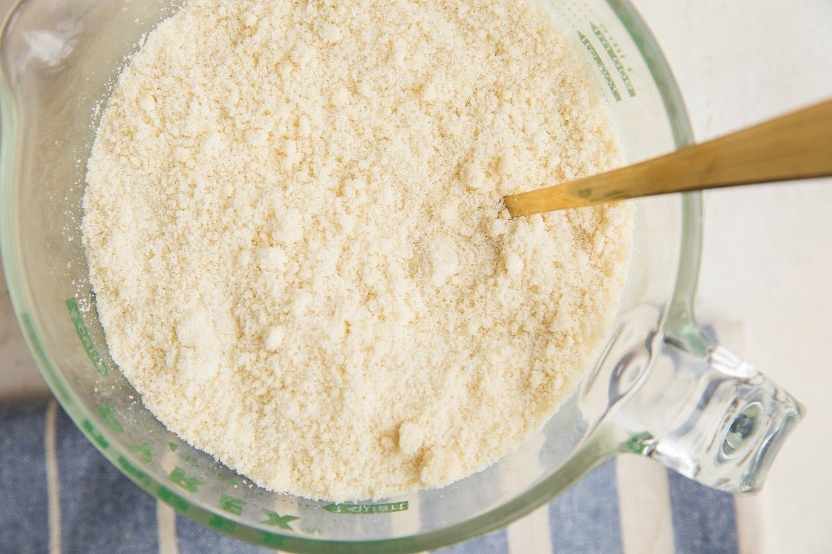 A glass measuring cup filled with almond flour, with a gold-colored spoon inside—perfect for preparing Keto Lemon Pound Cake. The cup sits on a blue and white striped cloth.