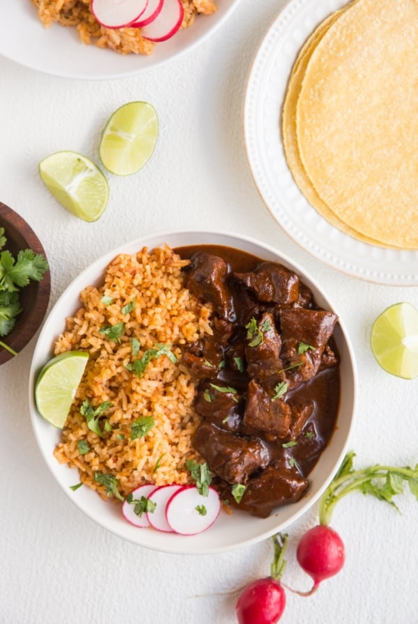 Bowl of chile colorado with Spanish rice and corn tortillas off to the side