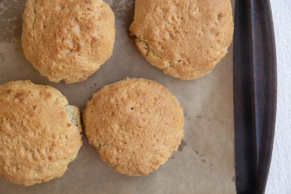Four golden-brown biscuits on a parchment-lined baking sheet, viewed from above. With their slightly rough texture, theyre perfect for a healthy strawberry shortcake or your favorite strawberry shortcake recipe.