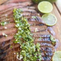 Finished skirt steak on a cutting board sliced up drizzled with chimichurri sauce.