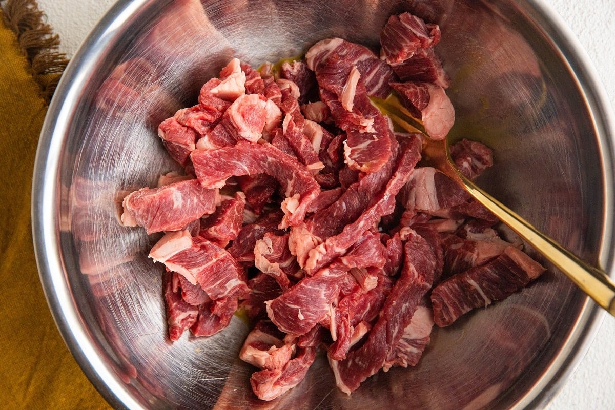 Sliced steak in a mixing bowl with beaten egg