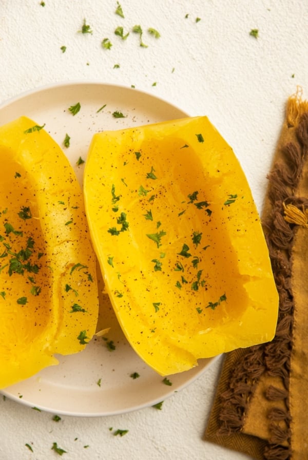 Cooked spaghetti squash on a white plate with a golden napkin to the side.