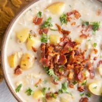 Close up top down photo of clam chowder in a bowl with crispy bacon and fresh parsley on top.