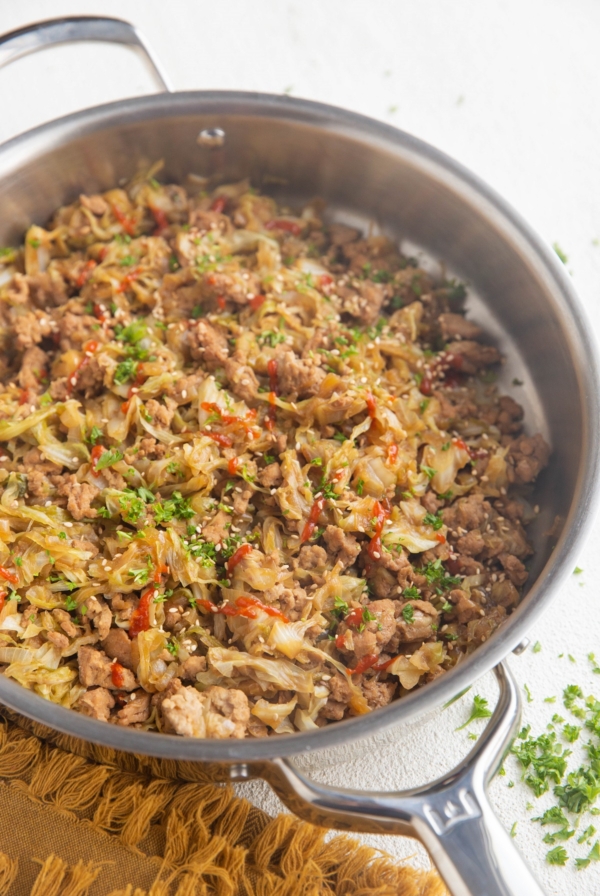 Stainless steel skillet full of ground turkey and cabbage with sriracha drizzled on top and sprinkled with parsley