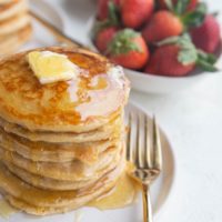 Stack of oatmeal protein pancakes with butter and syrup dripping down the side and butter on top.