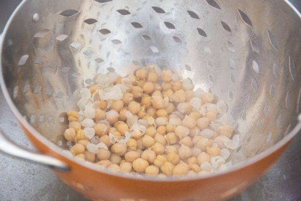 Boiled chickpeas in a colander with skins off, ready to be removed.