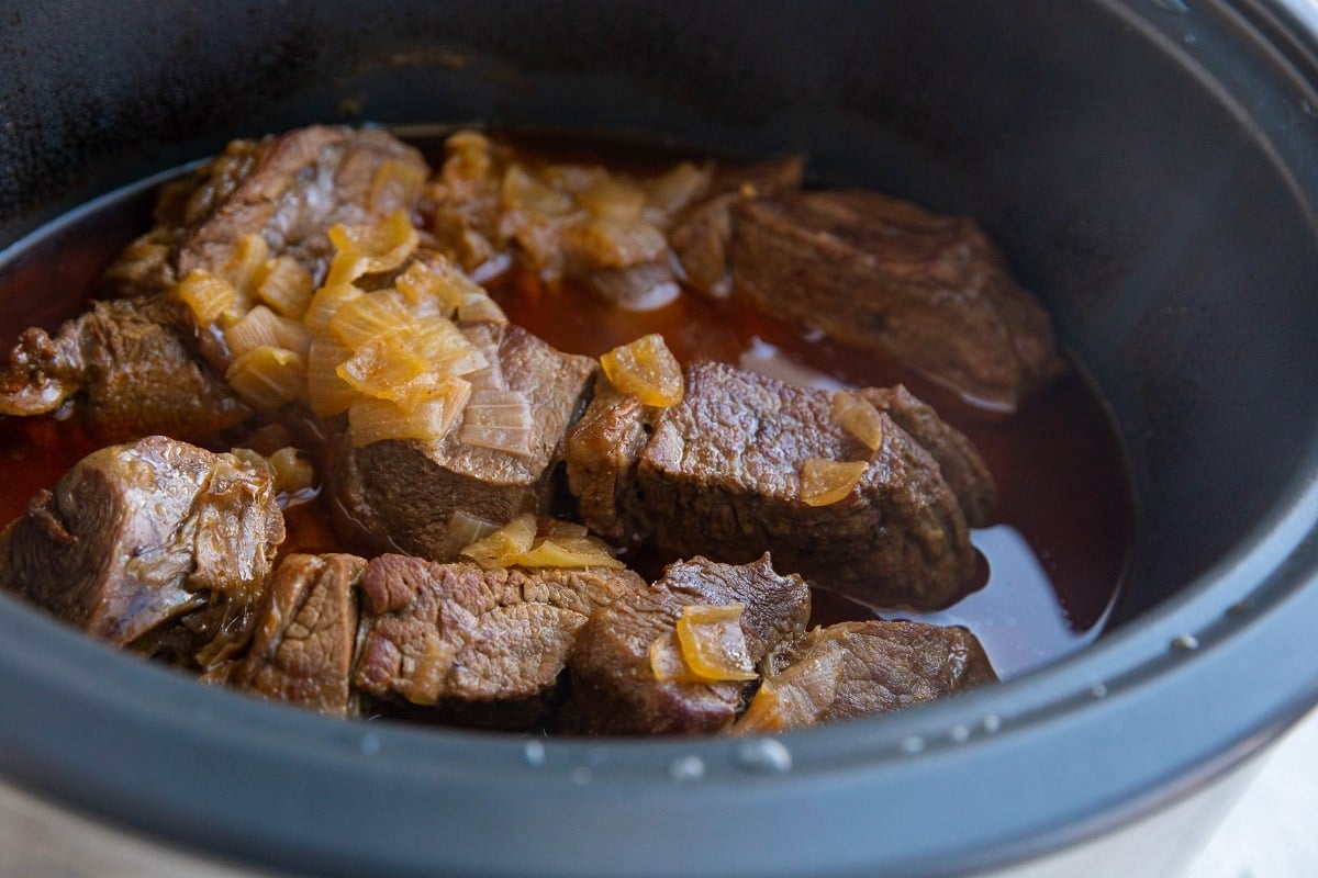 Cooked beef in a slow cooker with juices inside.