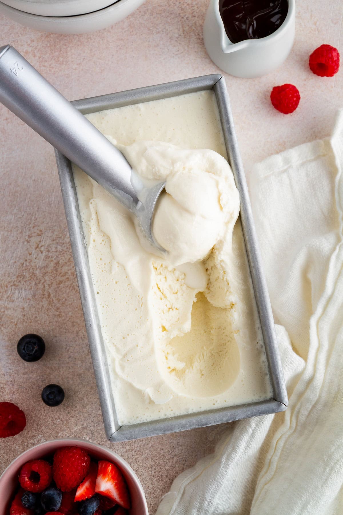 Homemade vanilla ice cream in a container with fresh berries and chocolate sauce to the side. Ready to serve and eat!