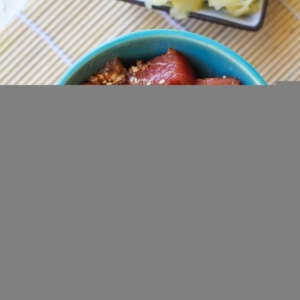 Ahi tuna poke in a teal colored bowl with chopsticks to the side and a bowl of pickled ginger. Ready to consume as an appetizer or as a main dish.
