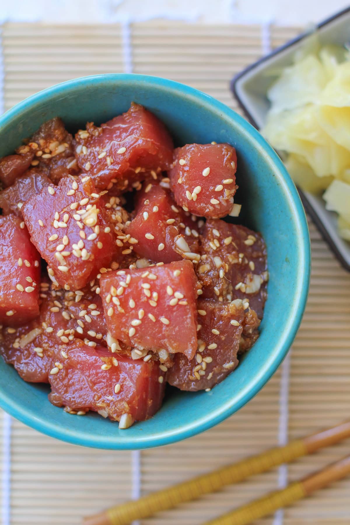Ahi Poke in a teal bowl with a small bowl of pickled ginger to the side with chopsticks. Ready to eat.