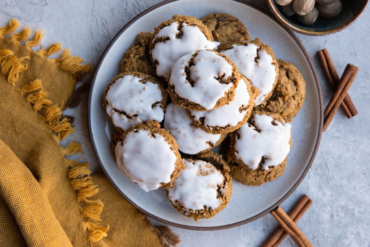 Plate of iced ginger molasses cookies with cinnamon sticks and nutmeg to the side and a golden napkin.