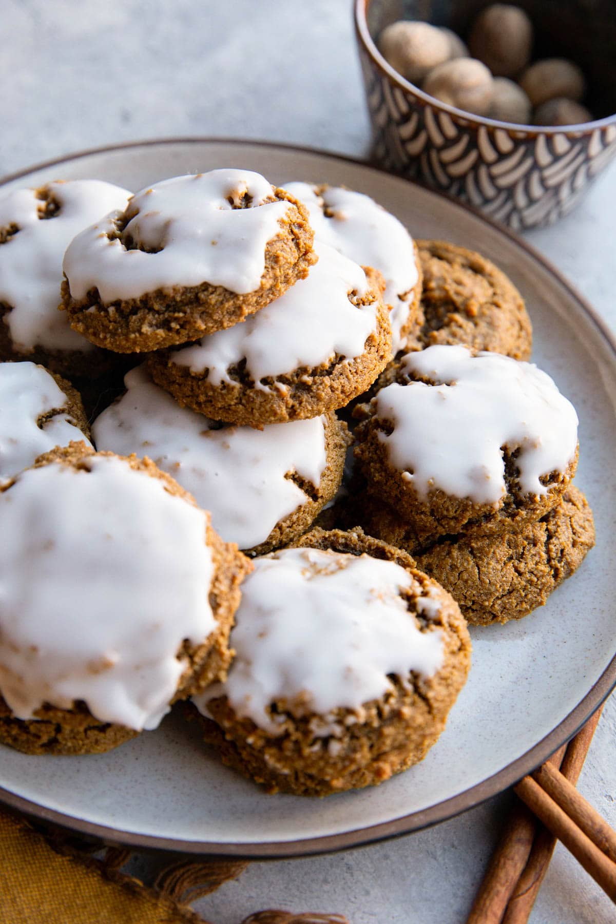 Plate of iced ginger molasses cookies with cinnamon sticks to the side and a small bowl of fresh nutmeg in the background.