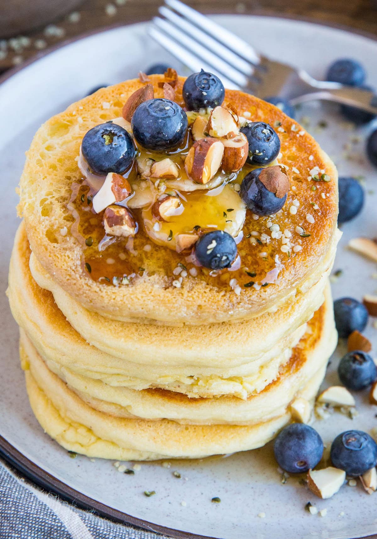Almond flour pancakes on a plate with blueberries and sliced banana with a drizzle of pure maple syrup and a sprinkle of chopped almonds, ready to eat
