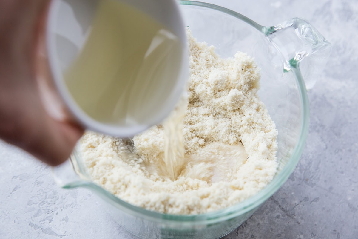 Pouring in the melted coconut oil to mix with almond flour to make gluten free pie crust.