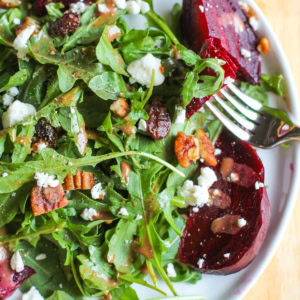 Arugula Beet Salad with pecans, cranberries, goat cheese and balsamic dressing on a white plate with a fork taking a bite.