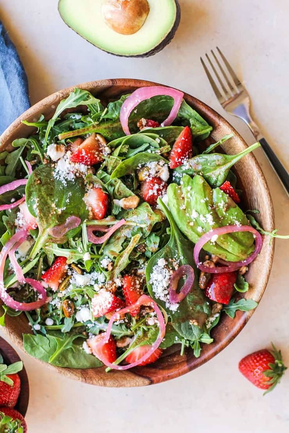 Wooden bowl of Strawberry Salad with pickled onions, feta, and strawberry vinaigrette with a bowl of fresh strawberries to the side and a fork.