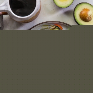 Three savory avocado pancakes on a plate with a poached egg on top and a side salad and a mug of coffee.