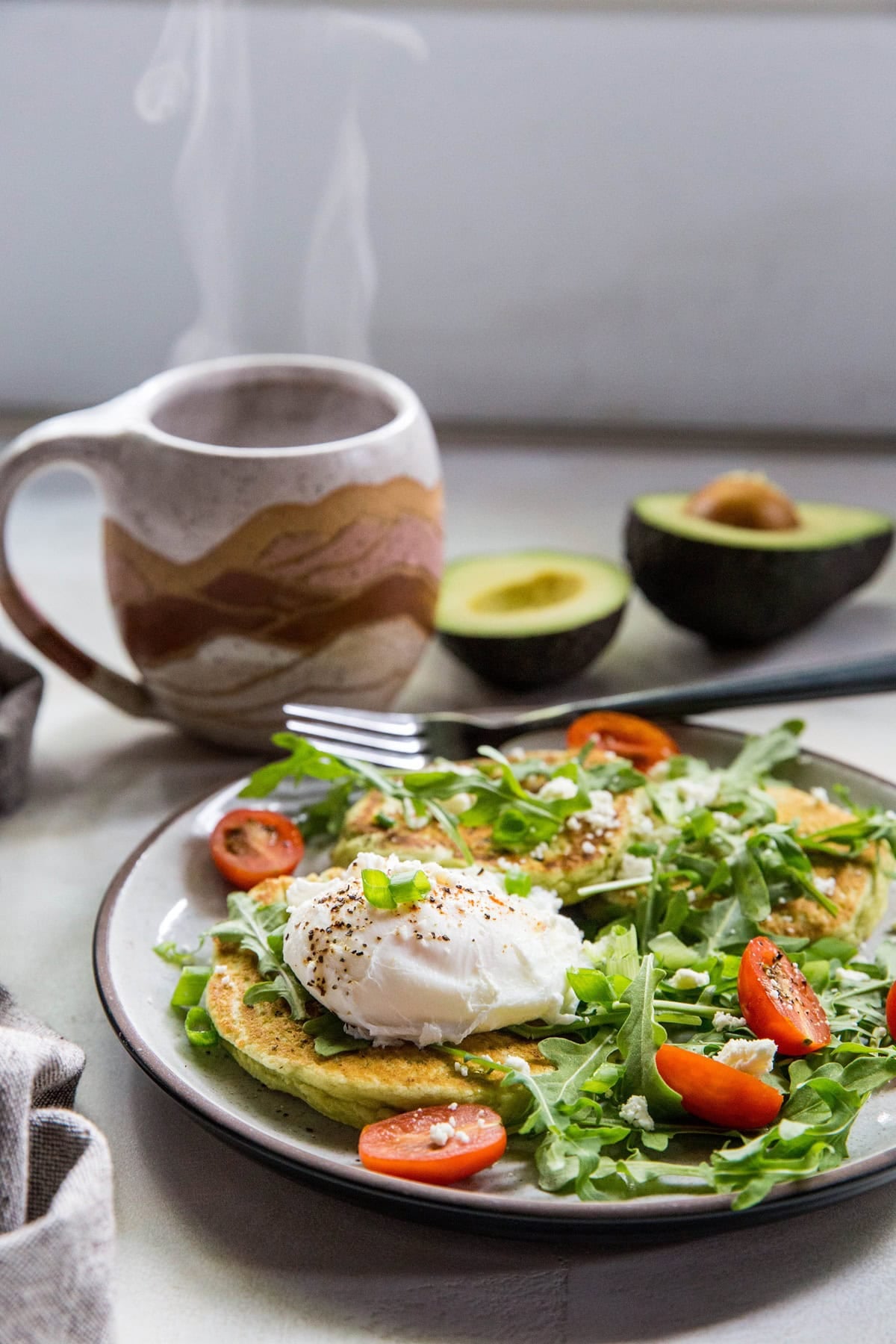 Plate with three avocado pancakes, an arugula salad, and a poached egg.