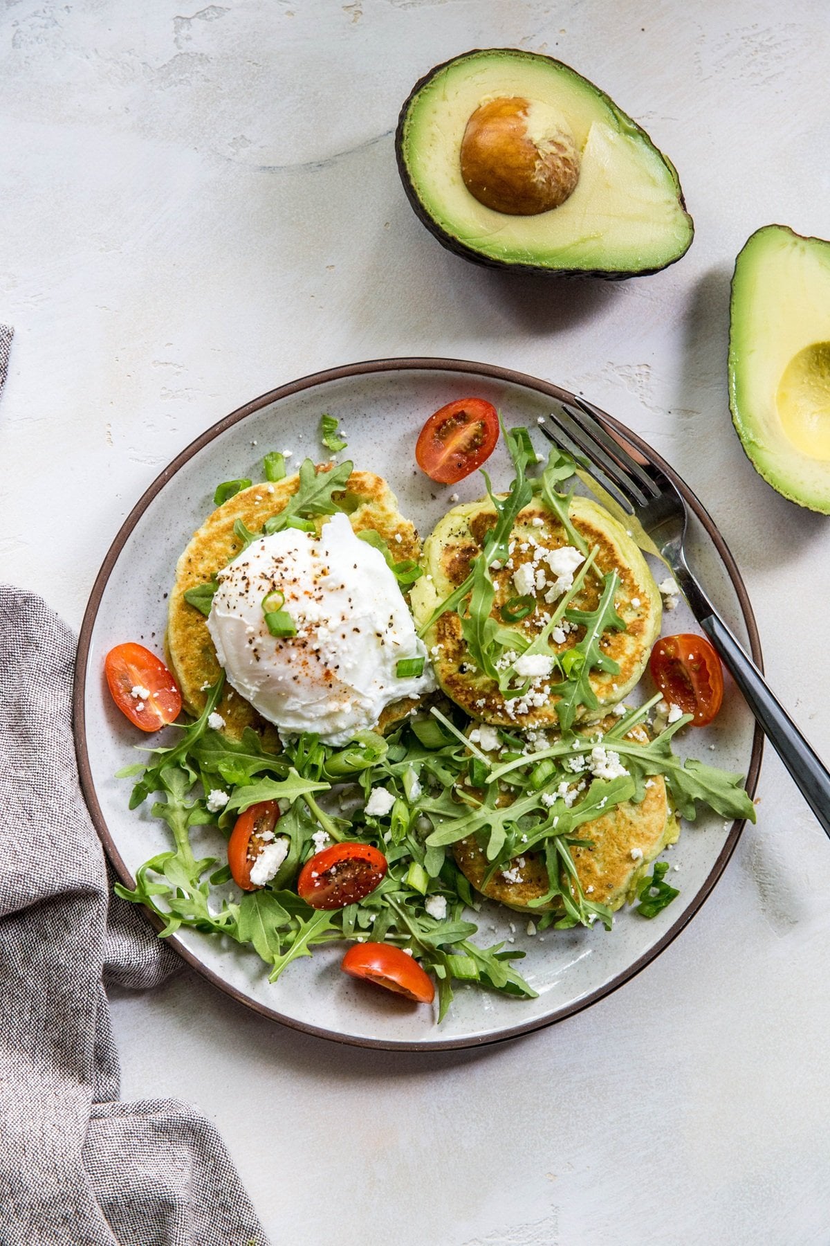 Plate of avocado pancakes with an egg on top and an arugula salad.
