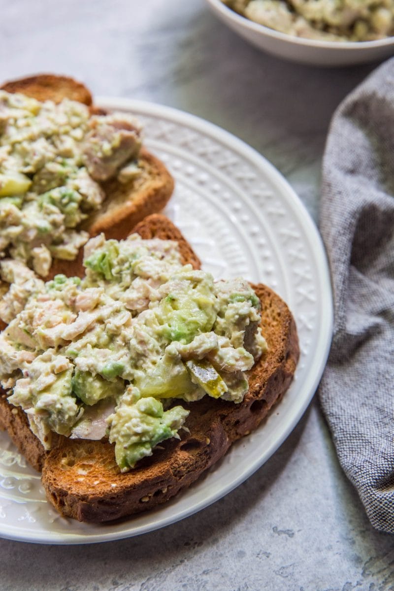 Avocado Tuna Salad on two slices of bread sitting on a white plate with a grey napkin to the side.