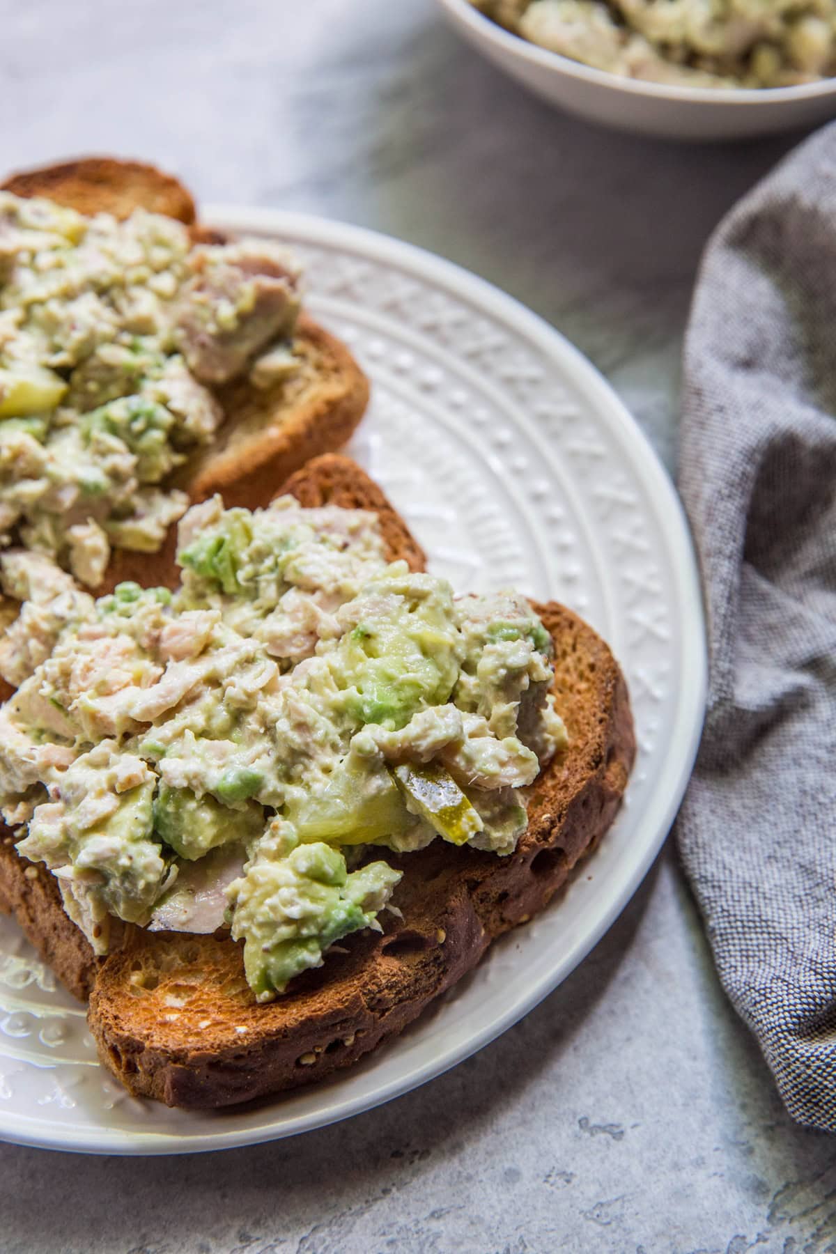 Avocado Tuna Salad on two slices of bread sitting on a white plate with a grey napkin to the side.