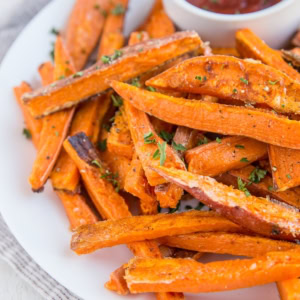 Plate of sweet potato fries with a small bowl of ketchup, sprinkled with chopped fresh parsley. Ready to serve.