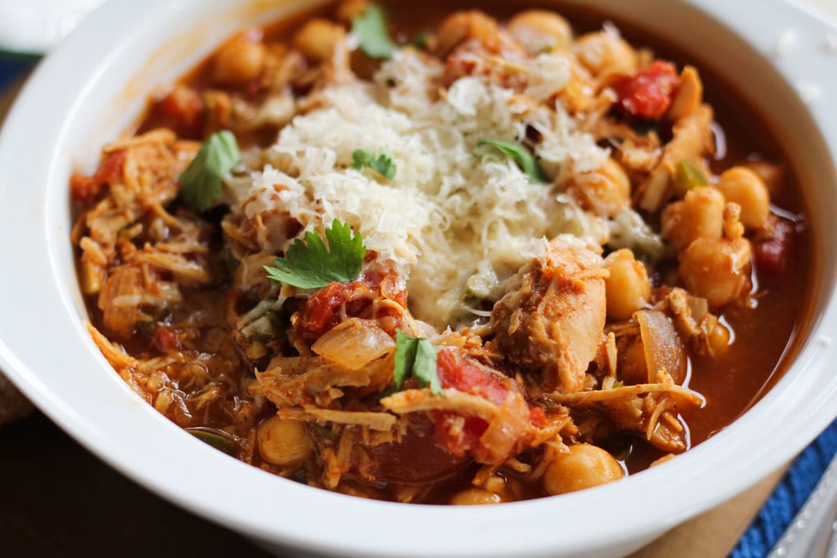 BBQ Pulled Chicken Chili in a white bowl with cheese and cilantro on top, ready to serve.