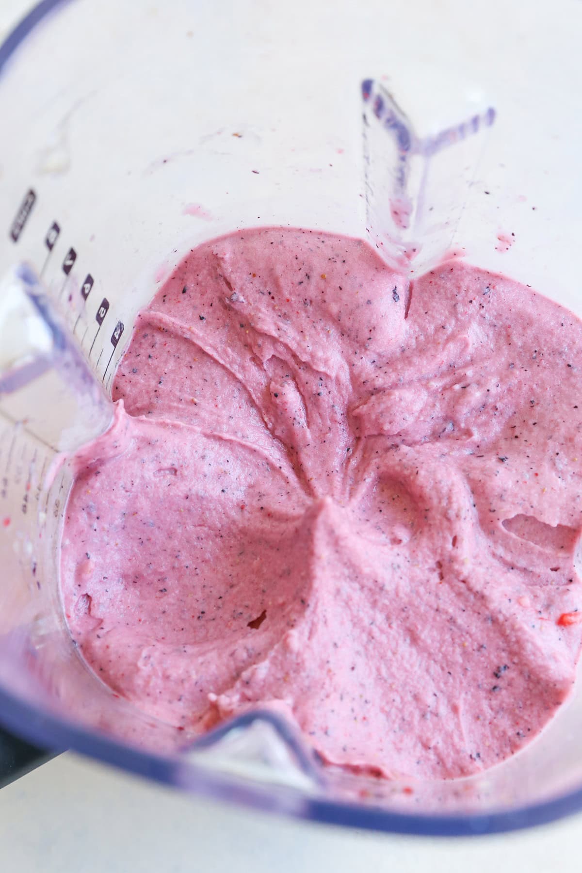 A close-up view of a blender filled with thick, creamy pink smoothie, swirled with small bits of fruit, perfect for making delicious nice cream.