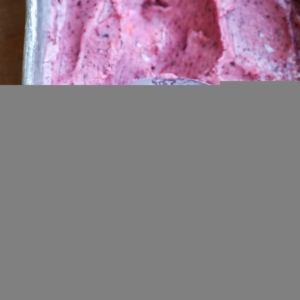 Loaf pan with berry nice cream inside and a ice cream scooper making a scoop to serve.