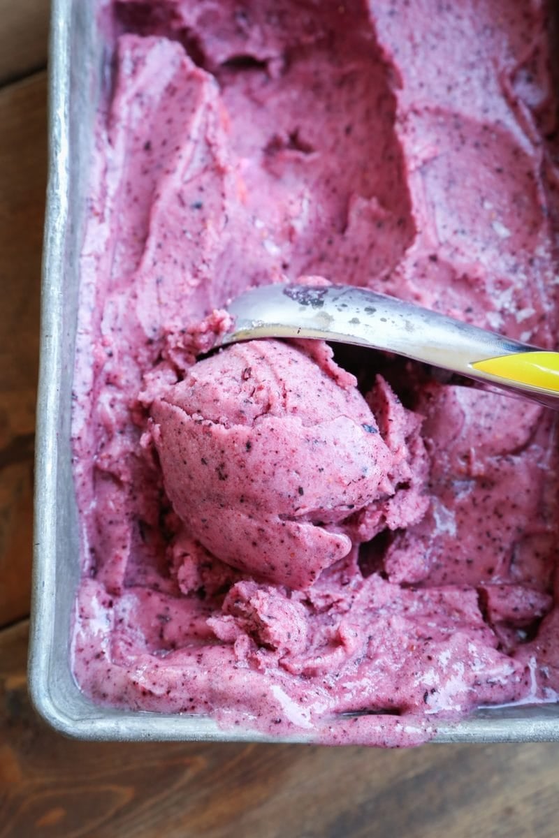 Loaf pan with berry nice cream inside and a ice cream scooper making a scoop to serve.