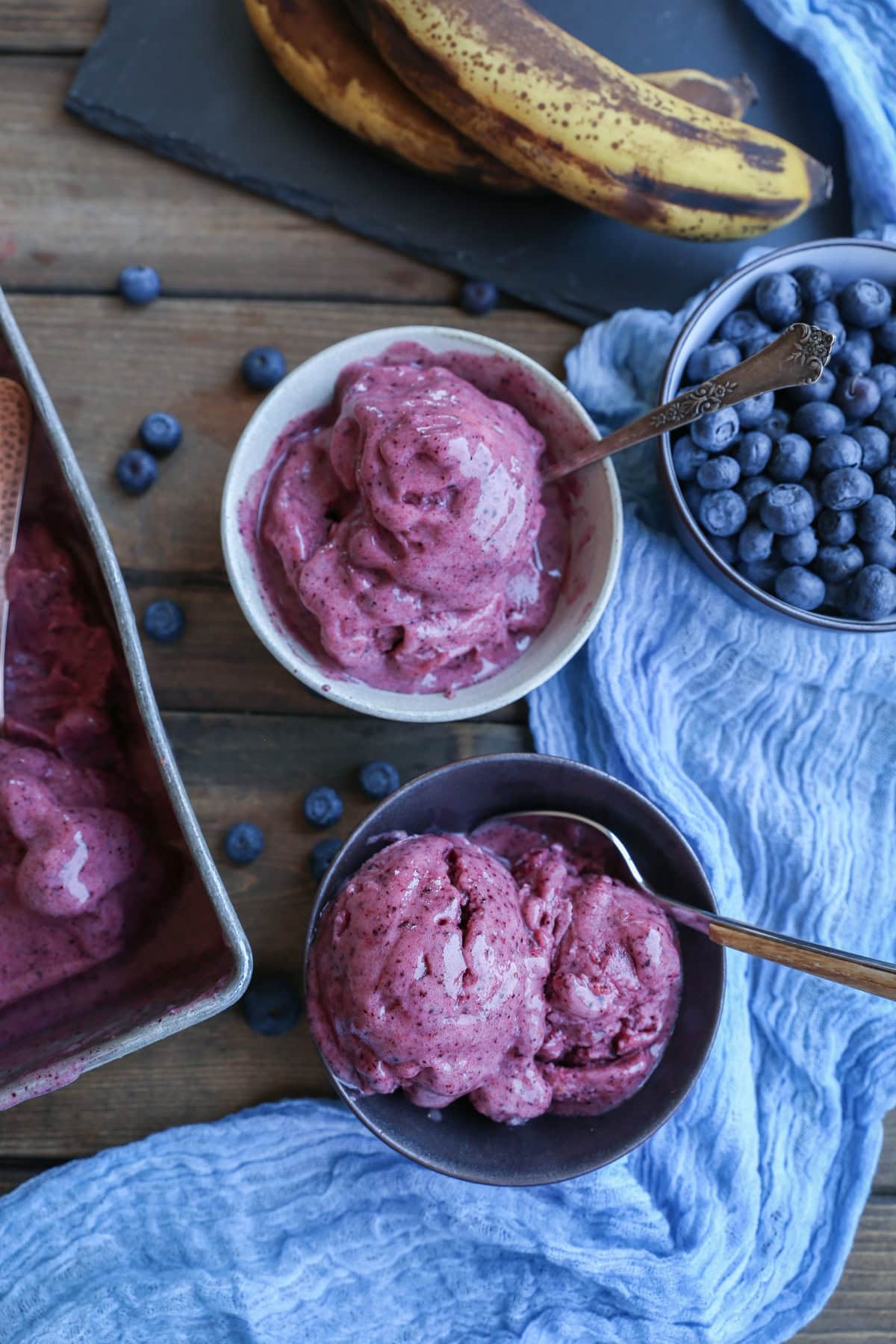 two bowls of berry ice cream with a blue napkin and fresh fruit to the side.