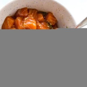 Bowl of salmon poke with a spoon in it on a white surface
